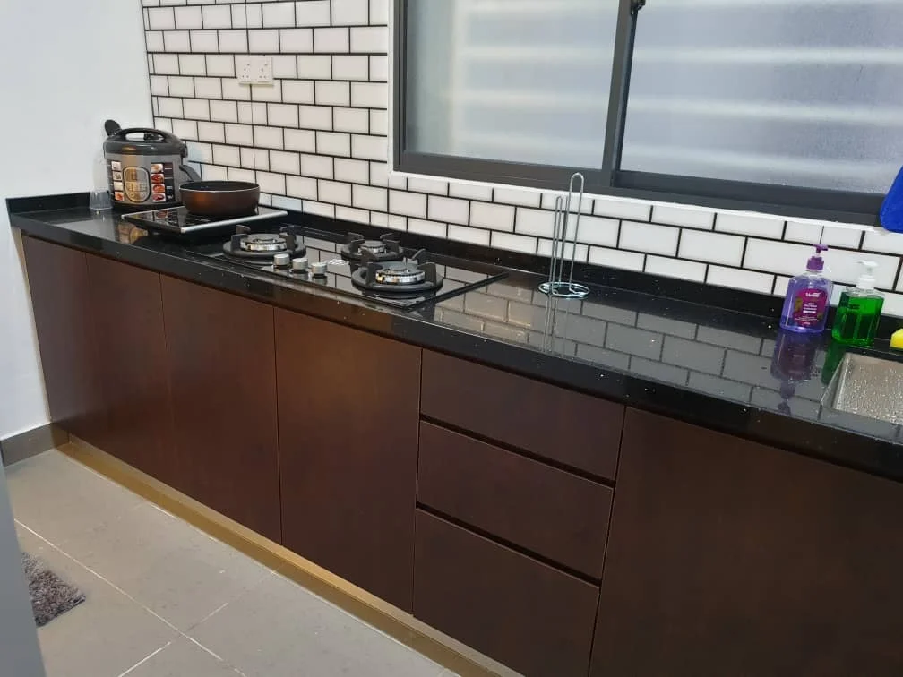 Kitchen features: black granite countertop, dark wood cabinetry, white subway tile backsplash, gas stove with two burners, stainless-steel sink, chrome pull-down faucet, built-in rice cooker, pantry cabinet, grey tile flooring, window with frosted glass, kitchen towel hanging, cleaning supplies on countertop; style: modern.